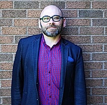 Professional man standing against brick wall in a suit jacket and purple shirt