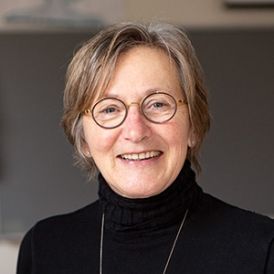 Head and shoulder shot of a middle age woman with round glasses and short brown hair in a black turtleneck. Dr. Maureen Coady.