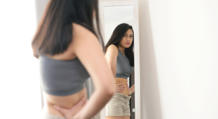 A young girl looking in a mirror squeezing her stomach.