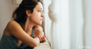 A woman looking sad as she looks out the window.