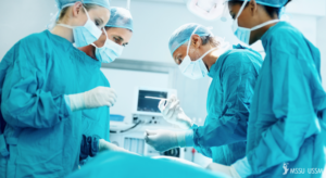 Surgeons in blue gowns leaning over hospital bed.