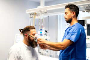 Nurse assisting patient by placing oxygen mask on his face in hospital room