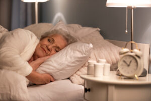 An older woman sleeping with pills beside on the bedside table.