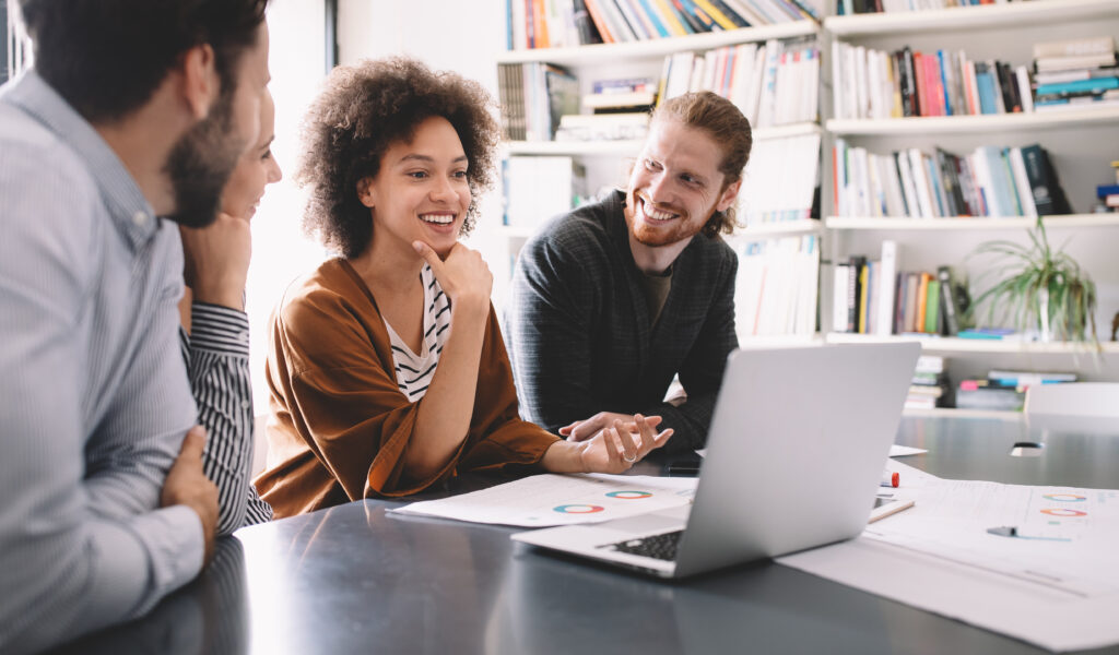 Three people around a laptop working together.