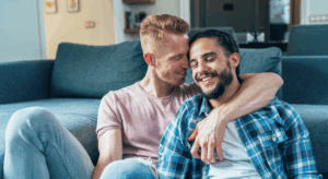 Two men cuddling by the couch together.