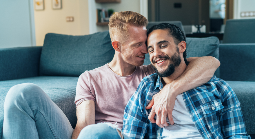 Two men cuddling by the couch together.