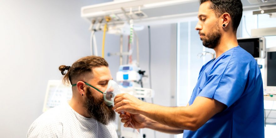 Nurse assisting patient by placing oxygen mask on his face in hospital room