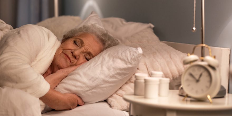 An older woman sleeping with pills beside on the bedside table.