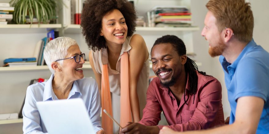 Group of diverse individuals looking at a laptop and smiling at each other.