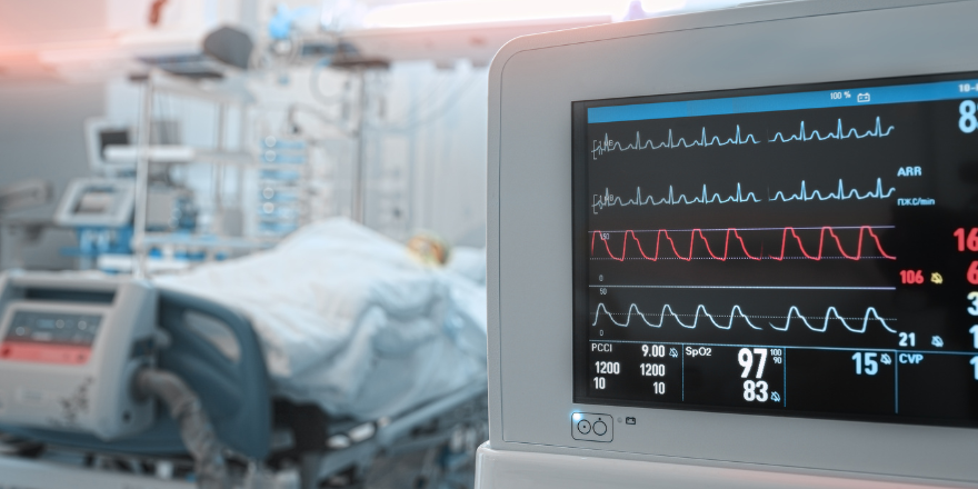 ICU monitor in the foreground with a hospital bed in the background.