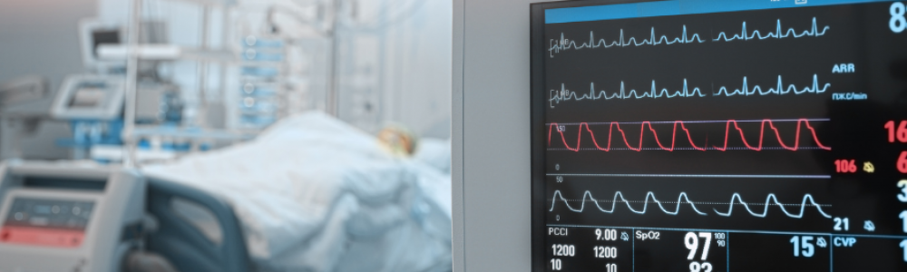 ICU monitor in the foreground with a hospital bed in the background.