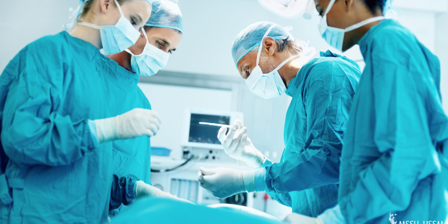 Surgeons in blue gowns leaning over hospital bed.