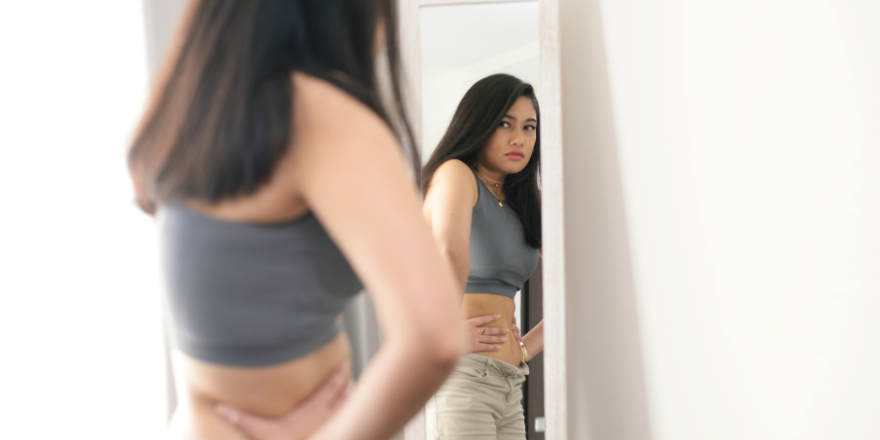 A young girl looking in a mirror squeezing her stomach.