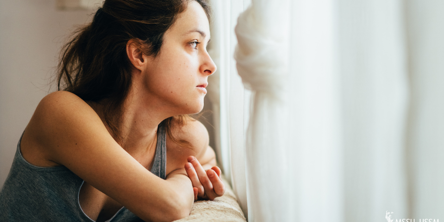 A woman looking sad as she looks out the window.