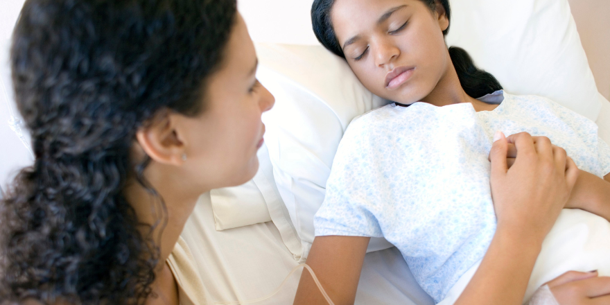 A mother at the bedside of her child sleeping in a hospital room.