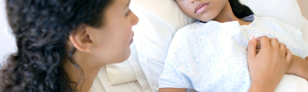 A mother at the bedside of her child sleeping in a hospital room.